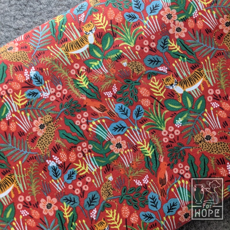 K&ouml;nnte beinhalten: Roter Stoff mit einem sich wiederholenden Muster aus Tigern, Blumen und Bl&auml;ttern. Der Stoff hat einen wei&szlig;en Hintergrund mit einem roten, gr&uuml;nen und gelben Muster. Der Stoff ist mit den Worten "For Hope" bedruckt.