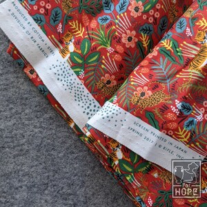 K&ouml;nnte beinhalten: Roter Stoff mit einem sich wiederholenden Muster aus Tigern, Leoparden, Blumen und Bl&auml;ttern. Der Stoff ist gefaltet und das Etikett lautet "Screen Printed in Japan, Spring 2017, Rifle, Inc."