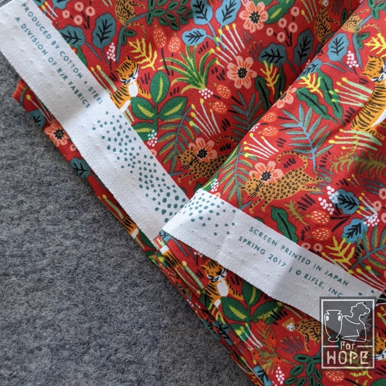 K&ouml;nnte beinhalten: Roter Stoff mit einem sich wiederholenden Muster aus Tigern, Leoparden, Blumen und Bl&auml;ttern. Der Stoff ist gefaltet und das Etikett lautet "Screen Printed in Japan, Spring 2017, Rifle, Inc."