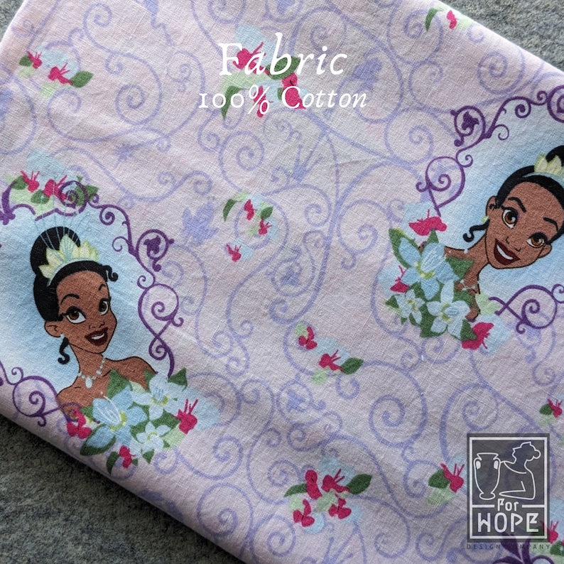 May include: Light purple fabric with a repeating pattern of a princess in a floral frame, with floral and swirl designs. The fabric is labeled "Fabric 100% Cotton". The design includes light blue, pink, and green accents.