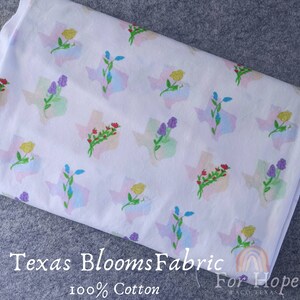 May include: White cotton fabric with a repeating pattern of the state of Texas outlined in pastel colors and a cluster of flowers in the center of each state. The text "Texas Blooms Fabric" and "100% Cotton" are printed at the bottom of the fabric.