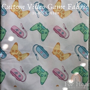 May include: White fabric with a repeating pattern of colorful video game controllers. The fabric is 100% cotton and says "Custom Video Game Fabric" and "For Hope Waco Texas" at the top and bottom.