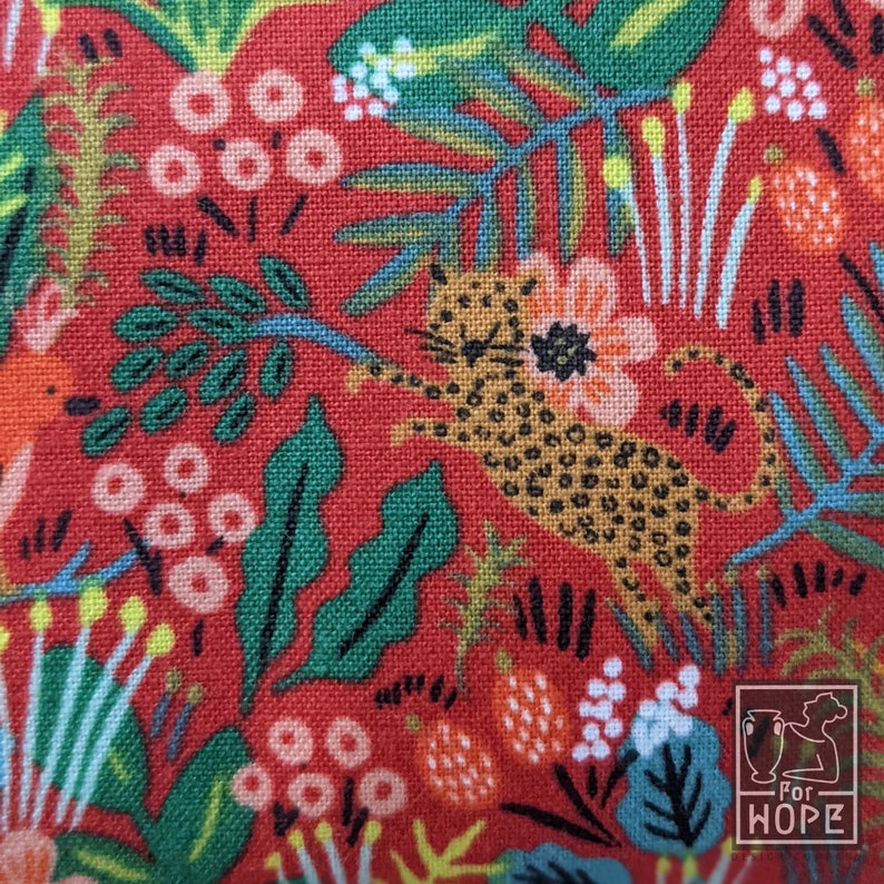 K&ouml;nnte beinhalten: Roter Stoff mit einem sich wiederholenden Muster aus gr&uuml;nen Bl&auml;ttern, orangefarbenen Bl&uuml;ten und einem gefleckten Leoparden. Der Stoff tr&auml;gt den Text "For Hope" in einem wei&szlig;en Kasten.