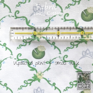 Peut inclure: Tissu en coton blanc avec un motif de vignes et de fleurs vertes. Le tissu est 100% coton et a un imprim&eacute; &agrave; petite &eacute;chelle. Une r&egrave;gle est plac&eacute;e sur le tissu pour montrer l'&eacute;chelle de l'impression. Le texte "Fabric 100% Cotton" et "Updated print - small scale" est visible sur le tissu.