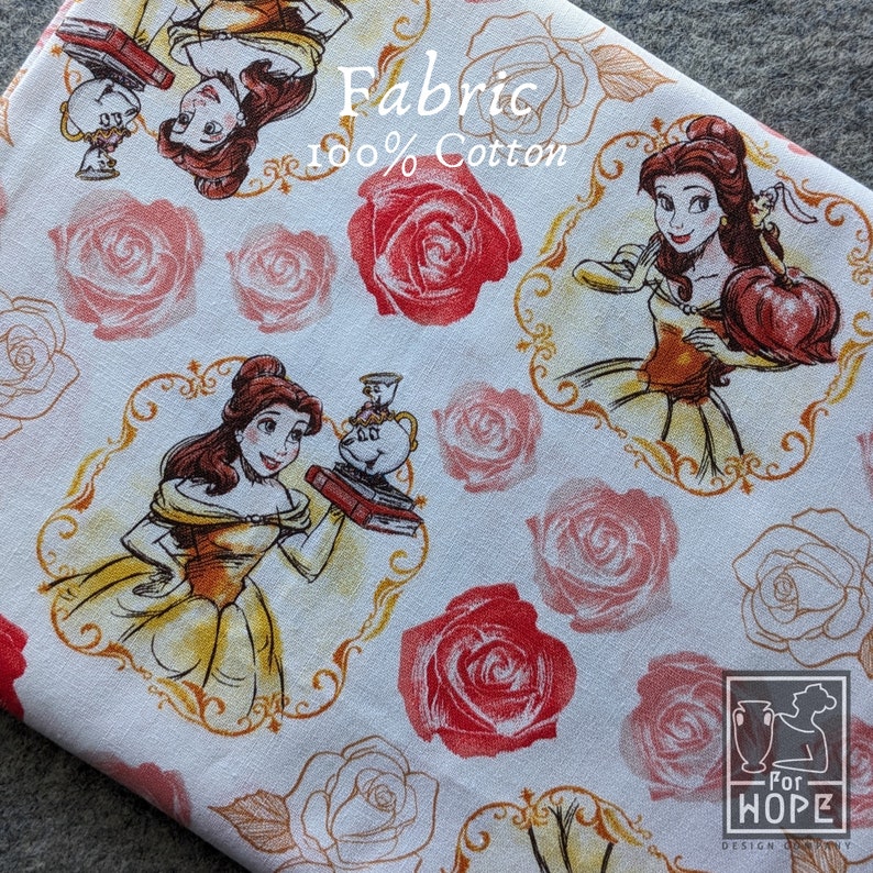 May include: White fabric with a repeating pattern featuring Belle from Beauty and the Beast, red roses, and gold frames. The fabric also has the text "Fabric 100% Cotton". The design is suitable for various sewing and crafting projects.