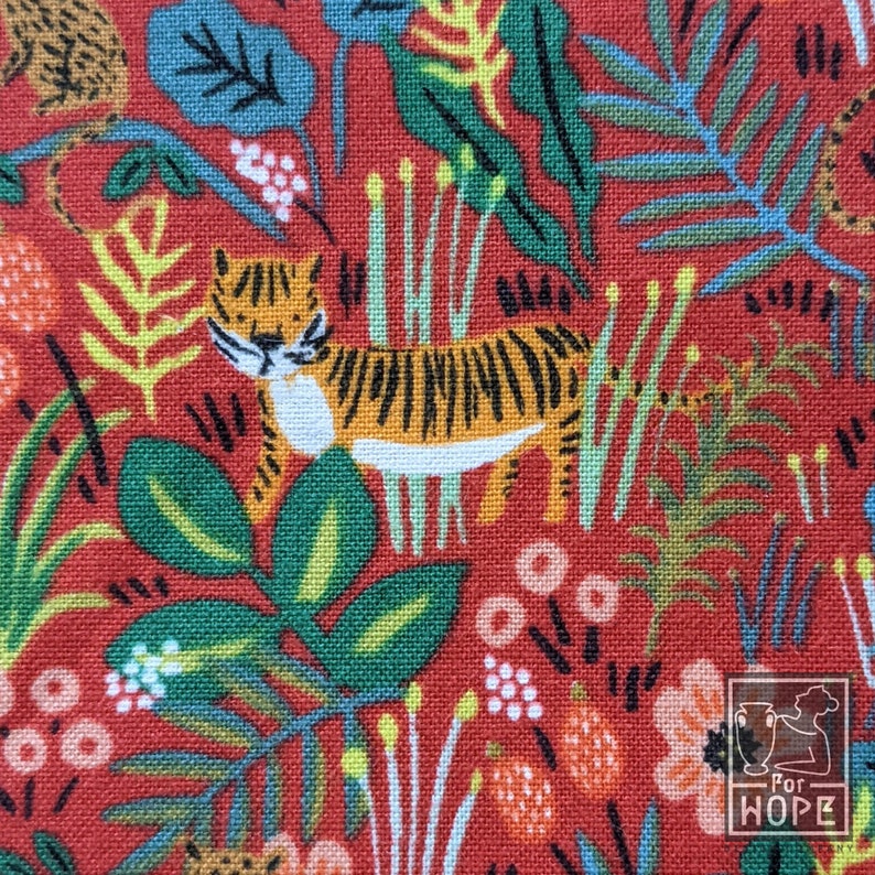 K&ouml;nnte beinhalten: Roter Stoff mit einem sich wiederholenden Muster aus Tigern, Bl&auml;ttern und Blumen. Die Tiger sind orange und schwarz mit wei&szlig;en Streifen. Die Bl&auml;tter sind gr&uuml;n und blau. Die Blumen sind wei&szlig;, rosa und orange.
