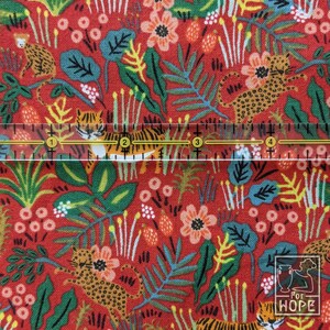 K&ouml;nnte beinhalten: Roter Stoff mit einem sich wiederholenden Muster aus Tigern, Blumen und Bl&auml;ttern. Der Stoff wird mit einem Lineal gemessen, das 10 cm anzeigt.