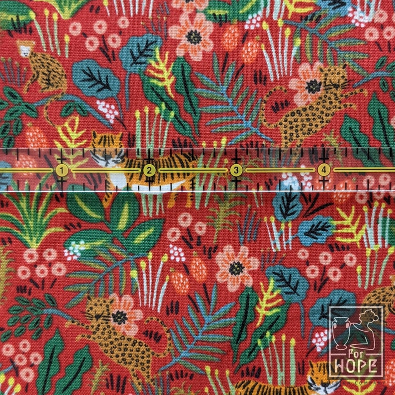 K&ouml;nnte beinhalten: Roter Stoff mit einem sich wiederholenden Muster aus Tigern, Blumen und Bl&auml;ttern. Der Stoff wird mit einem Lineal gemessen, das 10 cm anzeigt.