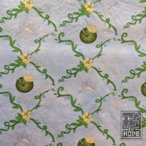 Peut inclure: Un tissu bleu clair avec un motif r&eacute;p&eacute;titif de vignes vertes, de fleurs jaunes et de n&eacute;nuphars verts. Le tissu a une texture subtile et un fond bleu clair.