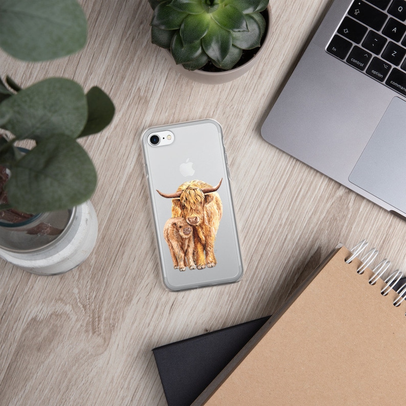 May include: A clear phone case with a watercolor illustration of a Highland cow and calf. The cow is brown with a long, shaggy coat and a white face. The calf is smaller and has a similar coat.