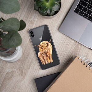 May include: A clear phone case with a watercolor illustration of a Highland cow and calf. The cow is brown and white with long, shaggy hair. The calf is smaller and has a more golden color.