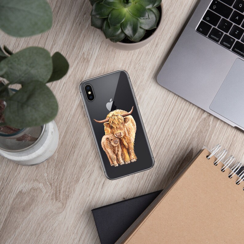 May include: A clear phone case with a watercolor illustration of a Highland cow and her calf. The cow is brown and white with long, shaggy hair. The calf is smaller and has a more reddish-brown color.