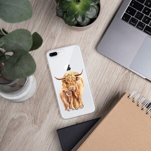 May include: A clear phone case with a watercolor illustration of a Highland cow and her calf. The cow is brown and white with long, shaggy hair. The calf is smaller and has a more reddish-brown color.