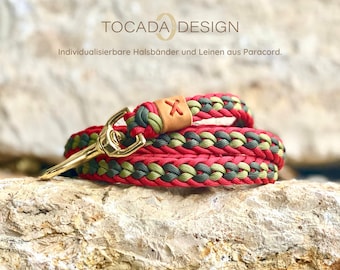 Op de afbeelding: Rode, groene en bruine paracord hondenriem met een gouden metalen sluiting. De riem is gevlochten en heeft een leren patch met een X erop. De tekst "TOCADADESIGN" en "Individualisierbare Halsbänder und Leinen aus Paracord." is zichtbaar op de achtergrond.