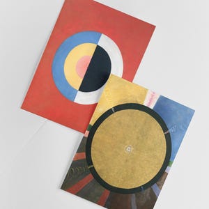 Puede incluir: Dos pinturas abstractas con c&iacute;rculos conc&eacute;ntricos. La primera pintura es roja con un c&iacute;rculo azul, amarillo, rosa y negro. La segunda pintura es amarilla con un c&iacute;rculo dorado rodeado por un anillo negro y un fondo colorido.