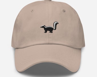 May include: A beige baseball cap with an embroidered black and white skunk on the front.