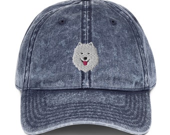May include: A blue denim baseball cap with a white embroidered dog face on the front.