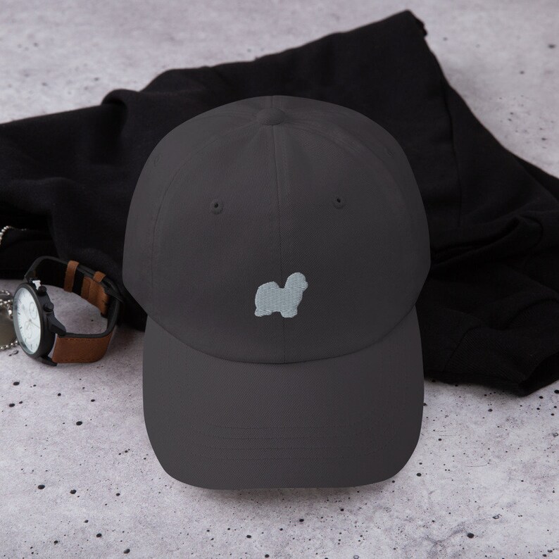 May include: A dark gray baseball cap with a light gray embroidered silhouette of a Shih Tzu dog.