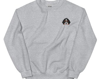 Puede incluir: Una sudadera gris con una pequeña imagen bordada de un perro de montaña de Berna en el pecho izquierdo.
