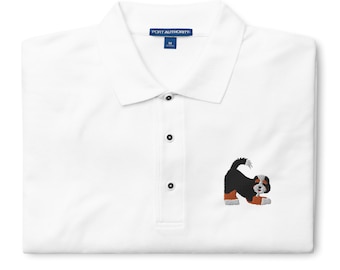 May include: White polo shirt with a small embroidered image of a Bernese Mountain Dog puppy on the left chest. The shirt has a blue label that says "PORT AUTHORITY" and a size "M".