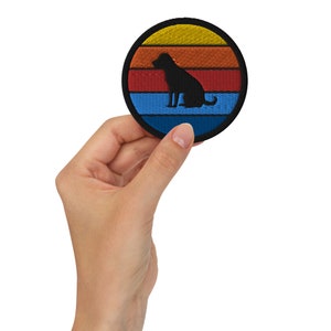 Peut inclure: Un patch rond brodé noir avec une silhouette de chien assis devant un coucher de soleil. Le coucher de soleil est composé de rayures jaunes, orange, rouges et bleues.