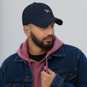May include: A navy blue baseball cap with a grey embroidered silhouette of a dog on the front.