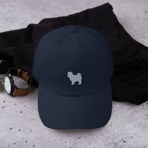 Può includere: Un cappello da baseball blu navy con una silhouette ricamata bianca di un cane Shih Tzu.