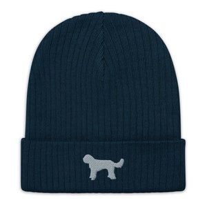 Puede incluir: Un gorro de punto azul oscuro con una silueta de perro bordada en gris claro.