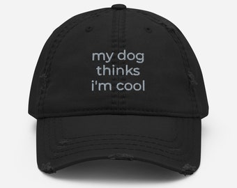 Może przedstawiać: Czarna, zniszczona czapka z daszkiem z białym haftem, na którym widnieje napis "my dog thinks i'm cool".