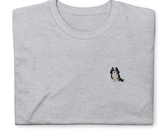 May include: A gray t-shirt with a small embroidered image of a black, white, and brown dog sitting on the left side of the shirt.
