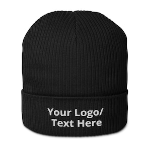 Puede incluir: Gorro de punto negro con una vuelta hacia abajo. La vuelta tiene bordado blanco que dice "Your Logo/Text Here".