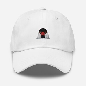 May include: White baseball cap with an embroidered image of a black and white bird with a red beak. The bird is looking directly at the viewer.