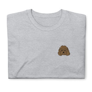 Könnte beinhalten: Ein graues T-Shirt mit einem gestickten braunen Pudel auf der linken Brust.