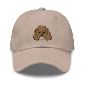 May include: A beige baseball cap with an embroidered brown and white poodle design.