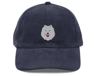 May include: A navy blue corduroy baseball cap with an embroidered white and gray dog face. The dog has a pink tongue sticking out.