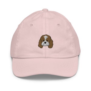 Puede incluir: Una gorra de béisbol rosa con un rostro de perro bordado en marrón y blanco.