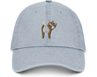 May include: A light blue denim baseball cap with an embroidered image of a brown and white Shiba Inu dog looking back over its shoulder.