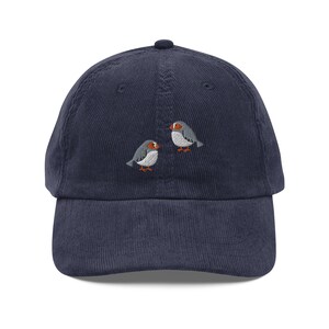Könnte beinhalten: Eine marineblaue Baseballkappe aus Cord mit einem gestickten Design aus zwei sich gegenüberstehenden grauen Vögeln.