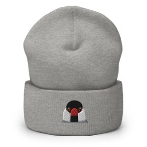 May include: Gray beanie with a black and white embroidered bird with a red beak. The bird is looking directly at the viewer.