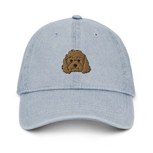 May include: A light blue denim baseball cap with an embroidered brown poodle on the front.