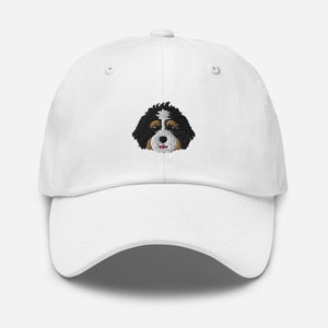 May include: White baseball cap with an embroidered image of a Bernese Mountain Dog's face.