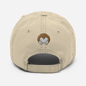 May include: A beige, distressed, baseball cap with an embroidered brown and white cartoon dog on the back.