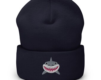 May include: A navy blue beanie with a white embroidered shark face with pink teeth.