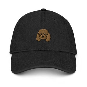 May include: A black denim baseball cap with an embroidered brown poodle face on the front.