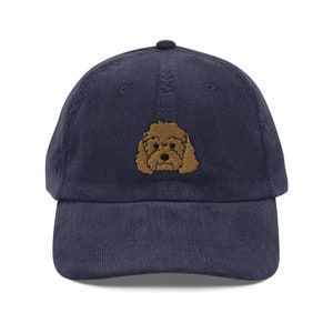 Könnte beinhalten: Eine marineblaue Baseballkappe aus Cord mit einem gestickten braunen Pudelgesicht.