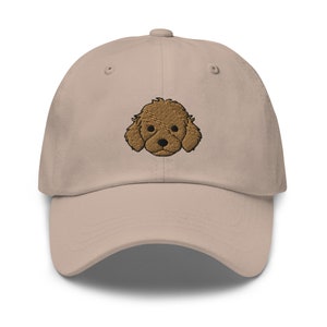 May include: A beige baseball cap with an embroidered brown poodle face.