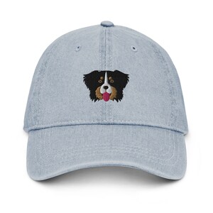 May include: A light blue denim baseball cap with an embroidered image of a black and white dog with brown ears and a pink tongue sticking out.