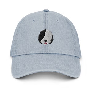 May include: A light blue denim baseball cap with an embroidered black and white dog face on the front.