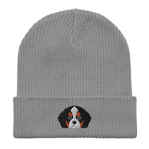 Puede incluir: Gorro de punto gris con una cara de perro bordada en negro, blanco y naranja.