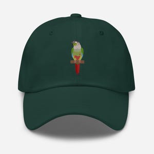 May include: A dark green baseball cap featuring a colorful illustration of a parrot perched on a branch. The parrot has green, red, white, and yellow details. The cap has a curved brim and a button on top.